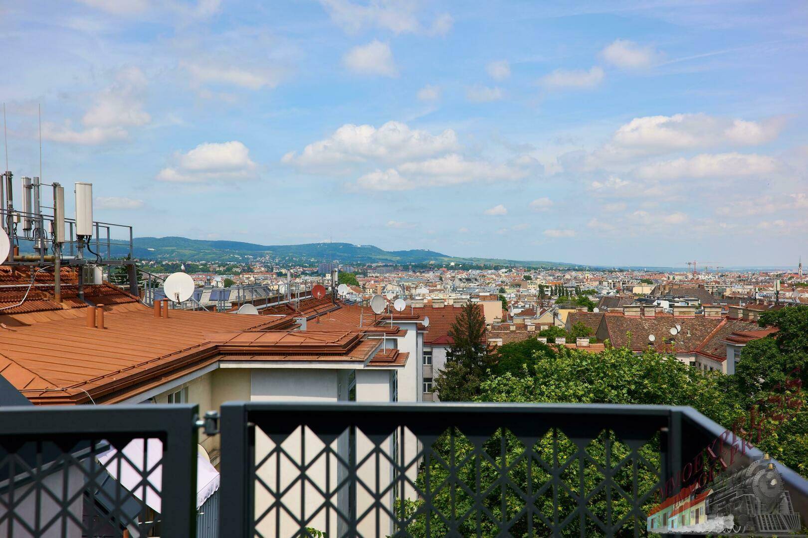 Panoramablick über die Stadt mit grünen Hügeln im Hintergrund und vielen Dächern.
