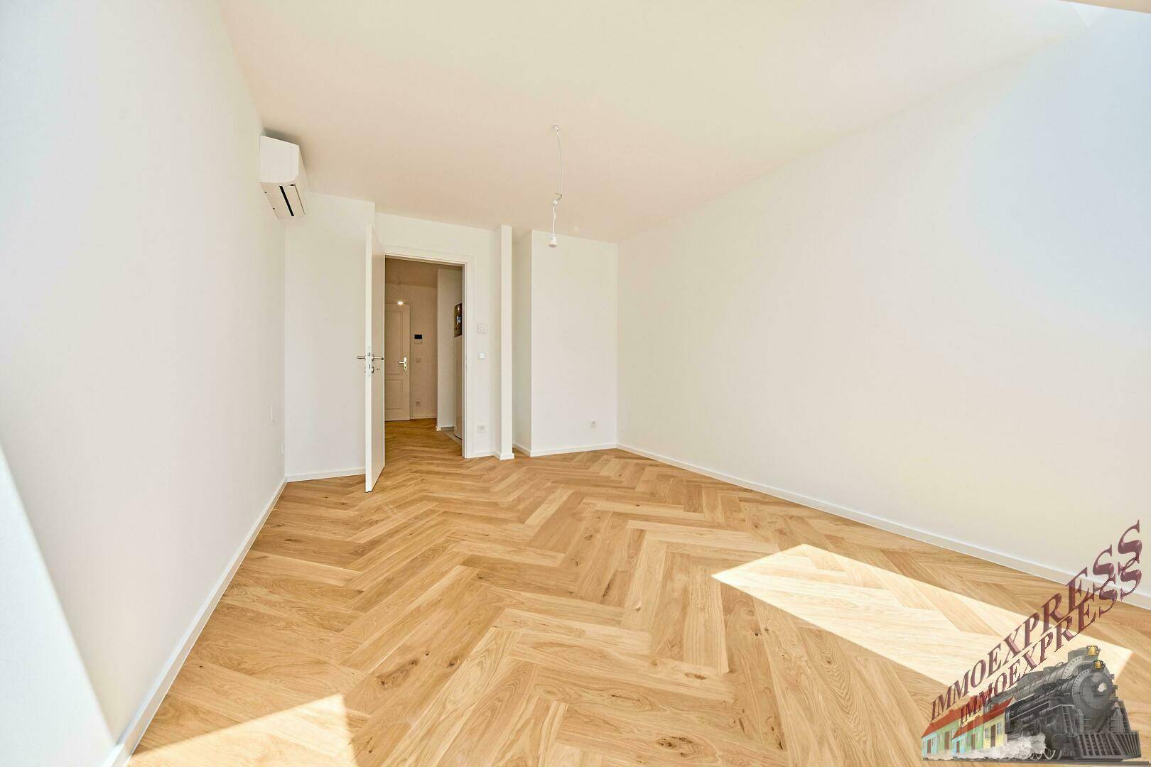 Helles Schlafzimmer mit Fischgrätparkett und Klimaanlage, bereit zur Einrichtung.