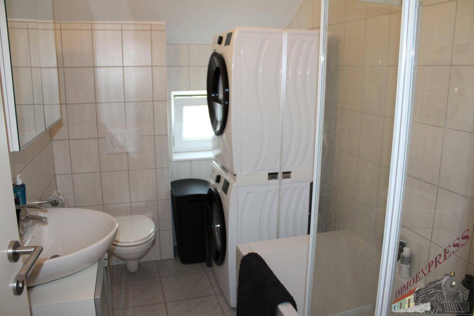 Badezimmer mit Waschmaschine, Trockner, Dusche und WC, hell gefliest und funktional.