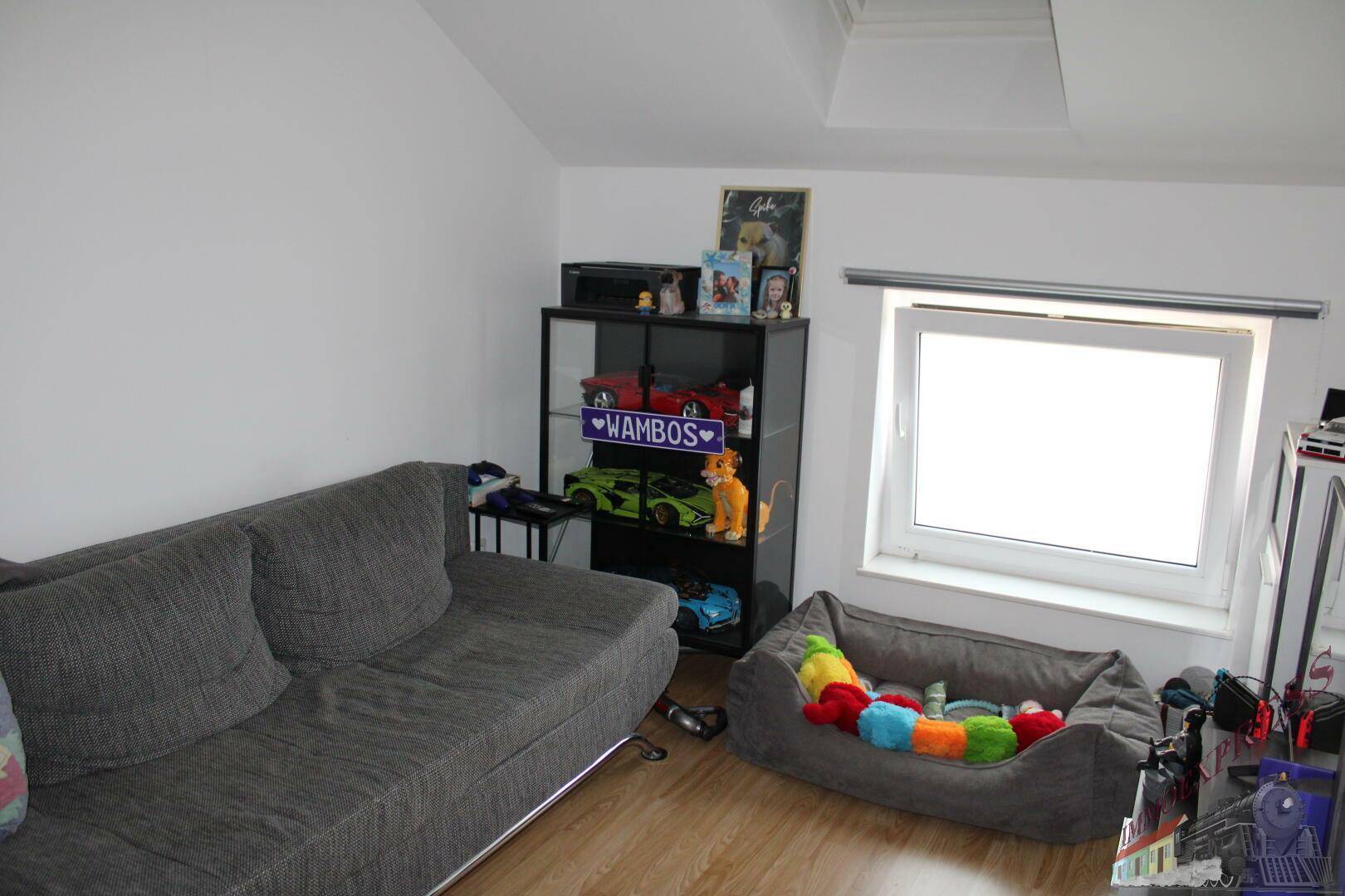 Wohnbereich im Dachgeschoss mit Sofa, Fenster und hellem Laminatboden.