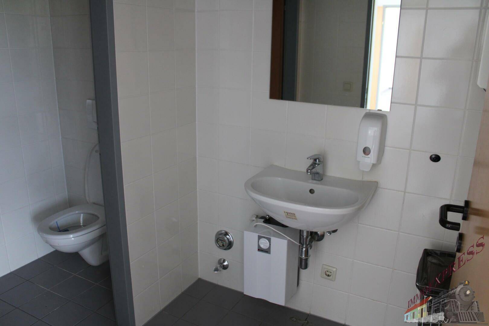 Sauberer Toilettenraum mit Waschbecken, Spiegel und weiß gefliesten Wänden.
