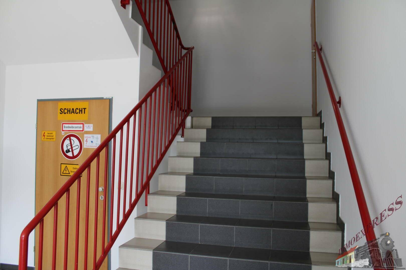 Geräumiges Treppenhaus mit robusten Fliesenstufen und roten Geländern, das verschiedene Etagen verbindet.