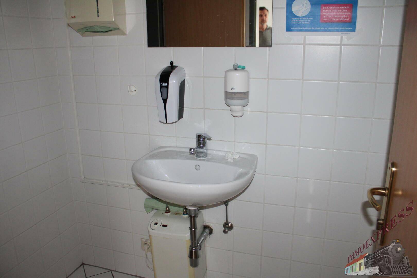 Kleiner Waschraum mit weiß gefliesten Wänden, einem Waschbecken und einem Spiegel.