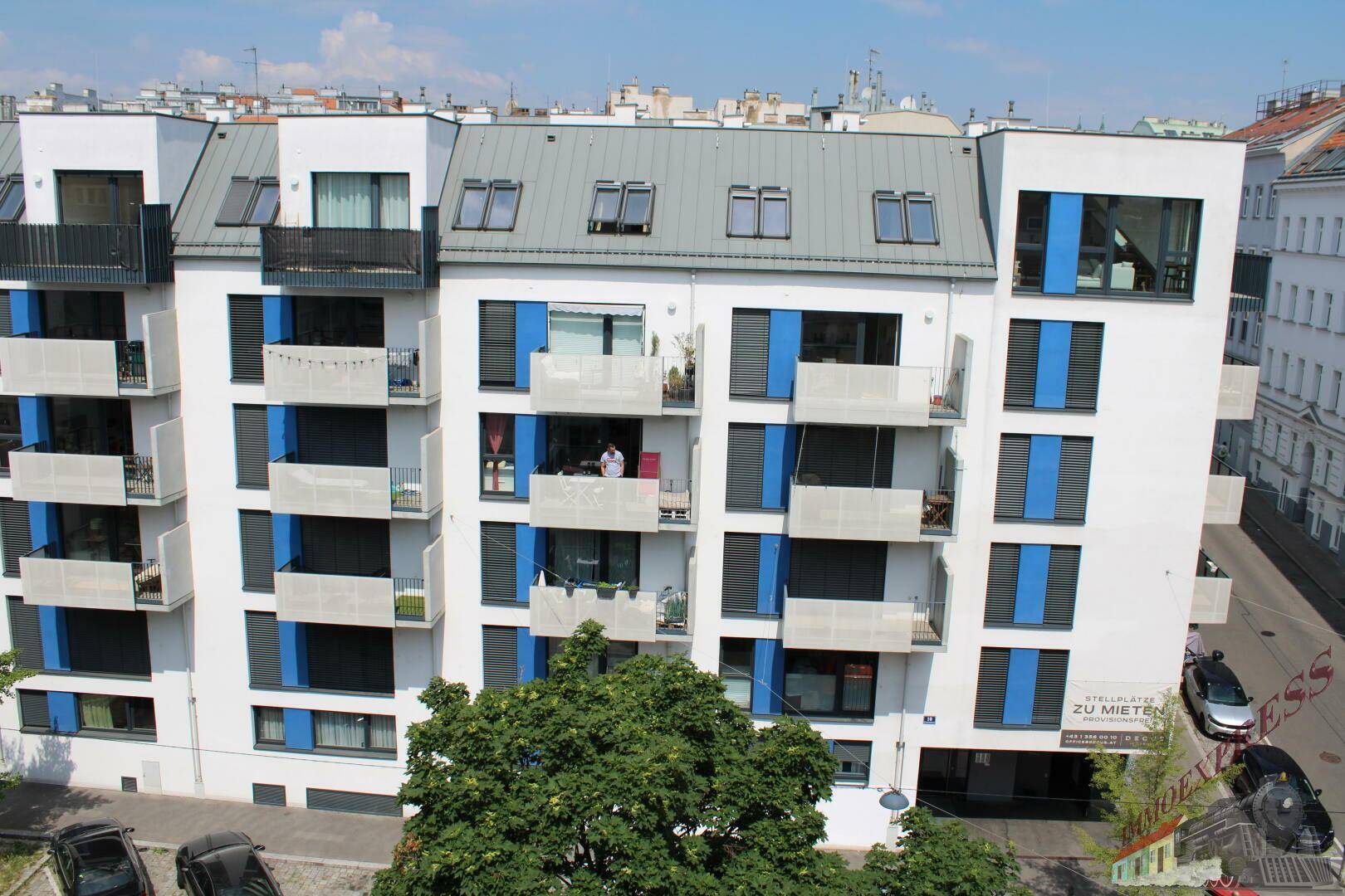 Moderne Wohnanlage mit weißer Fassade, blauen Akzenten und mehreren Balkonen unter blauem Himmel.