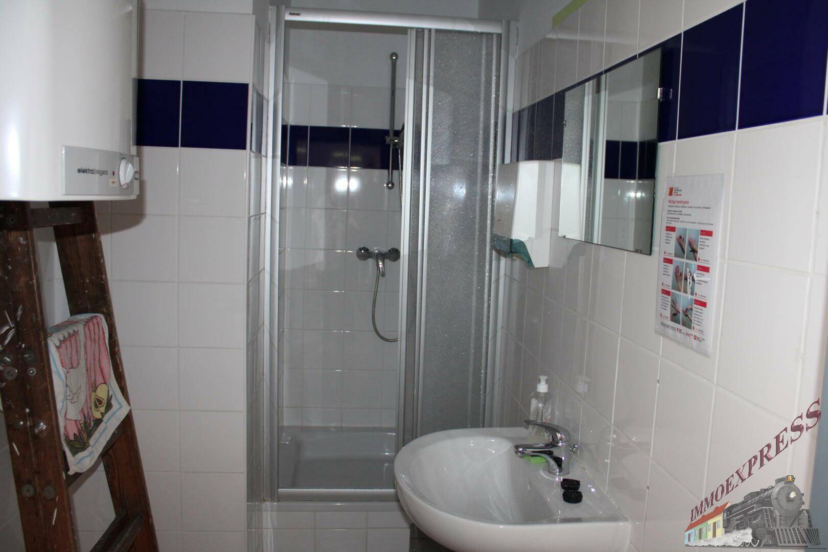 Badezimmer mit Duschkabine, Waschbecken und weißen Fliesen, akzentuiert durch blaue Streifen.