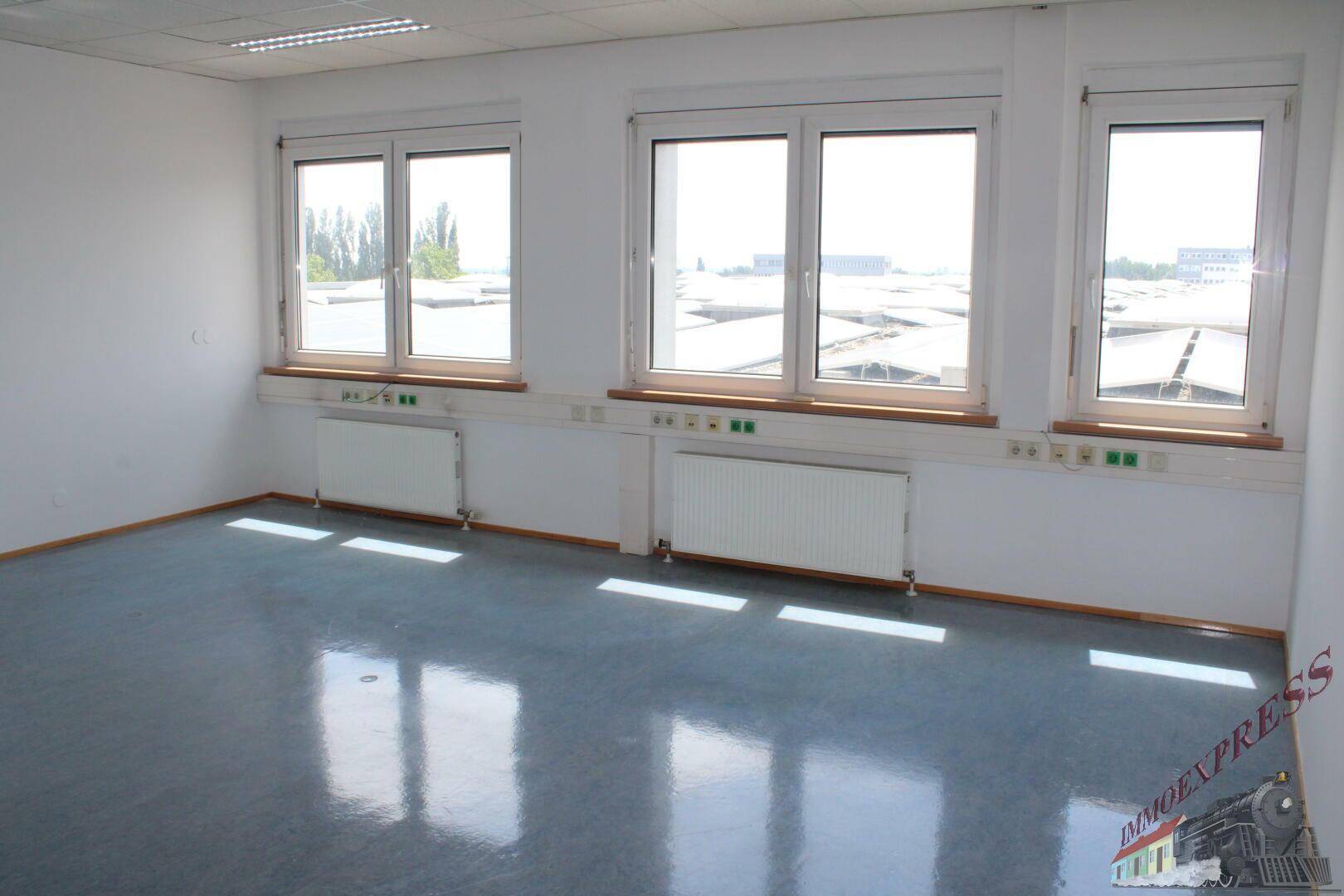 Helles Büro mit Vinylboden und einer Reihe von Fenstern, die einen Blick auf die Dächer bieten.