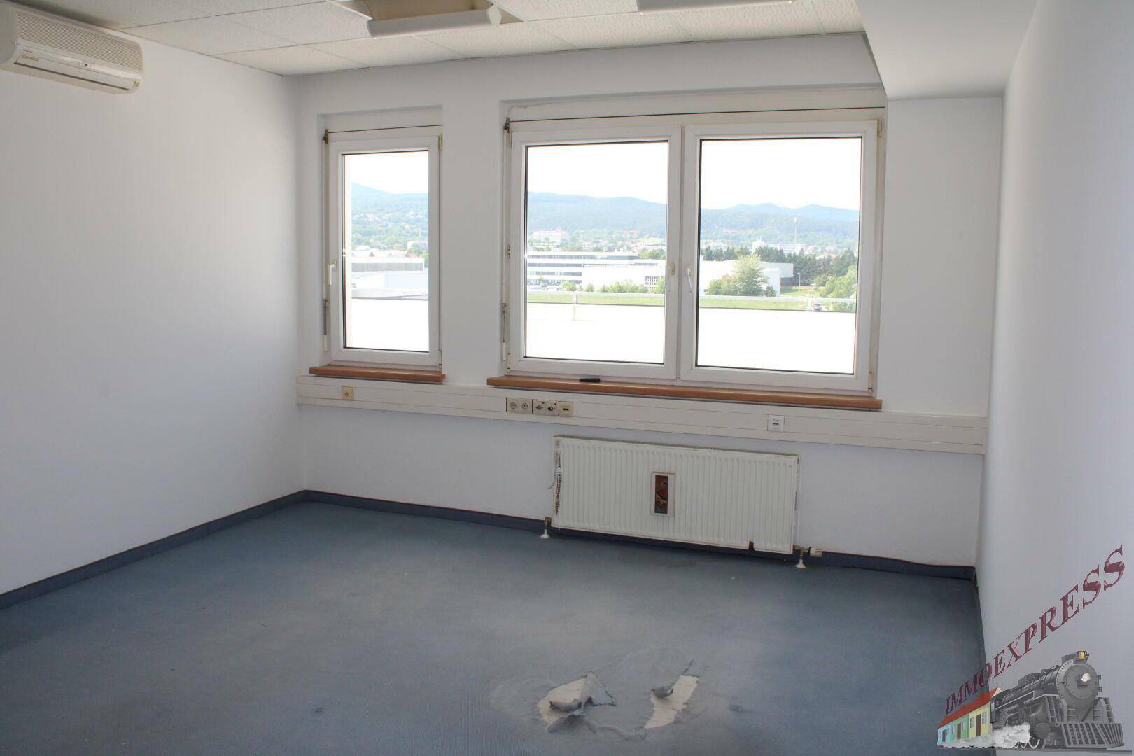 Leeres Büro mit Teppichboden, Klimaanlage und Fenstern mit Blick auf die Landschaft.