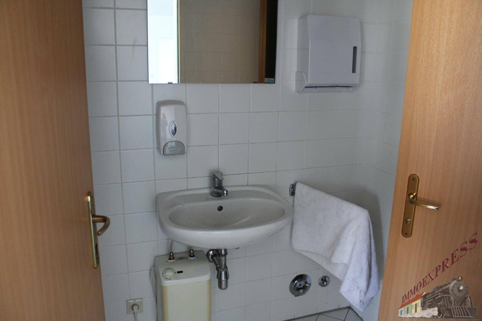 Kleines Badezimmer mit weiß gefliesten Wänden, Waschbecken und Spiegel.