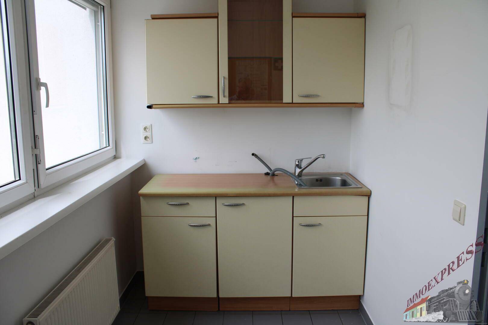 Kleine Küchenzeile mit Spüle, Unterschränken und einem Fenster, ideal für einen Pausenraum.