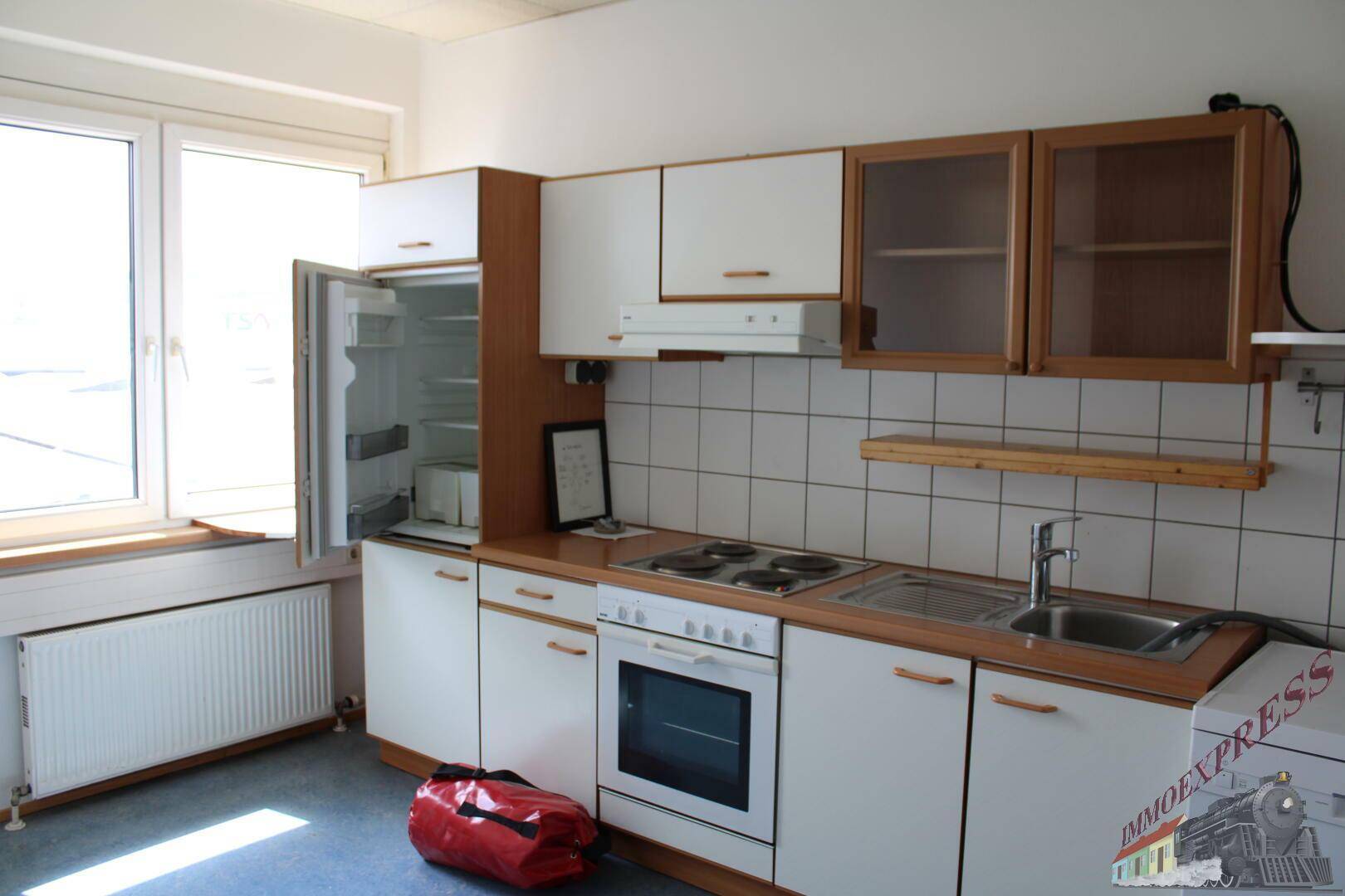 Funktionale Küche mit weißen Schränken, Holztheke und integrierten Geräten neben einem Fenster.