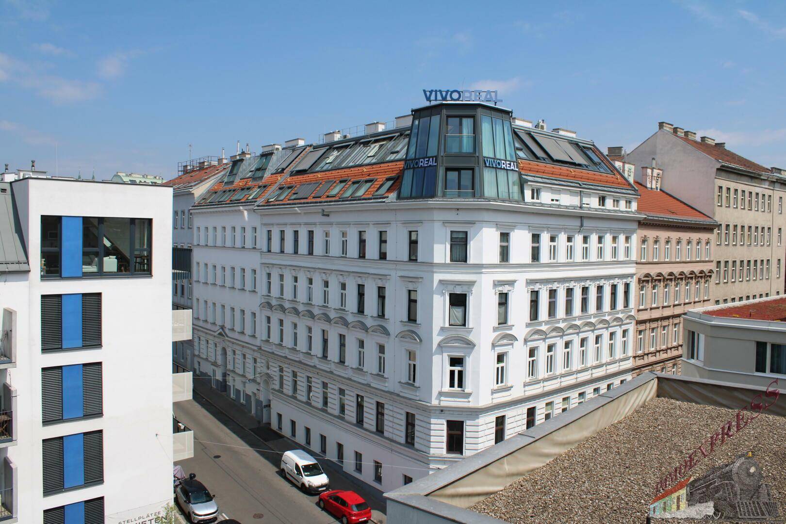 Historisches Gebäude mit moderner Dachaufstockung und vielen Fenstern in einer städtischen Umgebung.