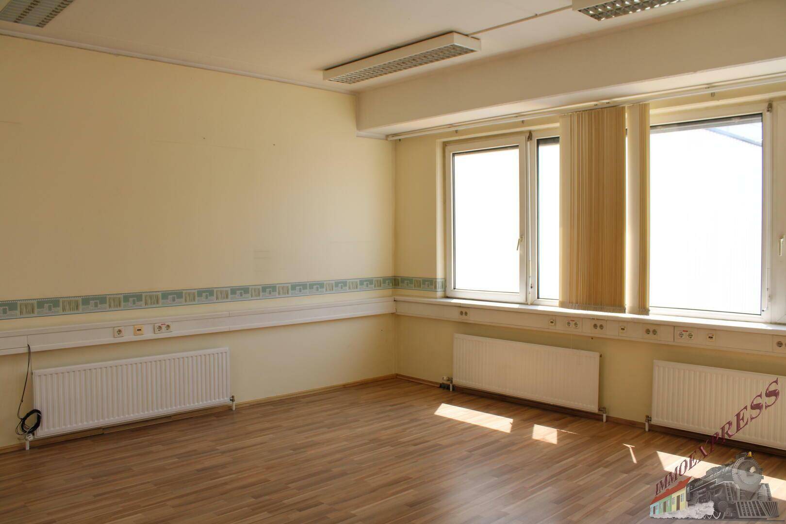 Geräumiges Büro mit Holzfußboden, großen Fenstern und Jalousien für Sonnenschutz.