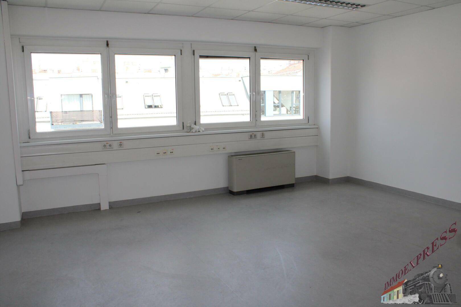 Geräumiges Büro mit großen Fenstern, die viel Tageslicht hereinlassen und einen Blick auf Dächer bieten.