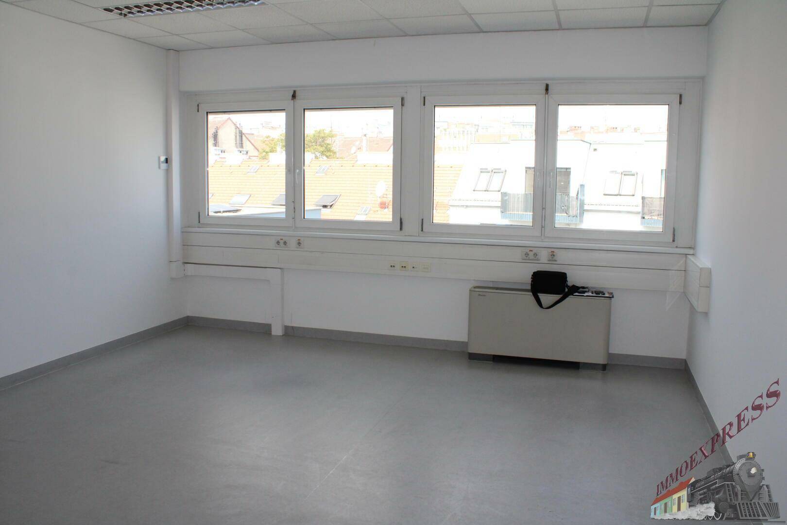 Helles Büro mit großen Fenstern, die viel Tageslicht hereinlassen und einen Blick auf Dächer bieten.