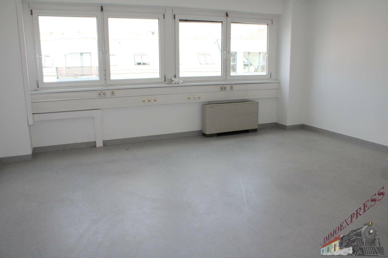 Leeres Büro mit großen Fenstern und einem Heizkörper unter der Fensterbank, bereit zur Einrichtung.