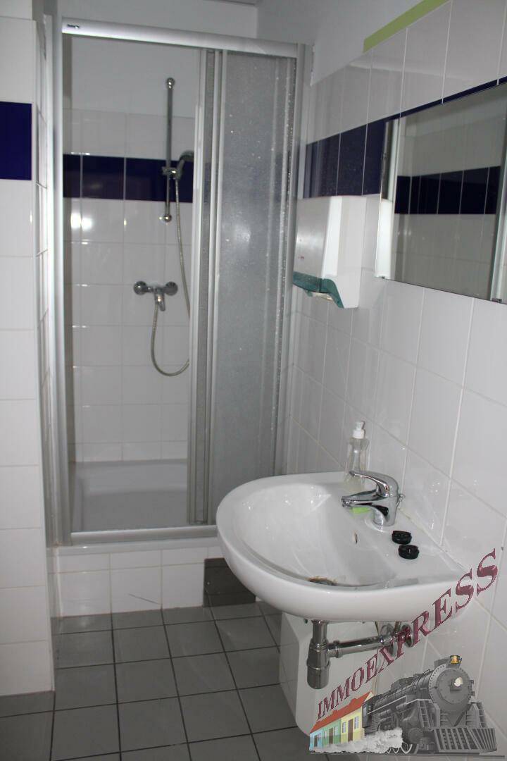 Badezimmer mit Duschkabine und Waschbecken, weißen und blauen Fliesen sowie grauem Boden.