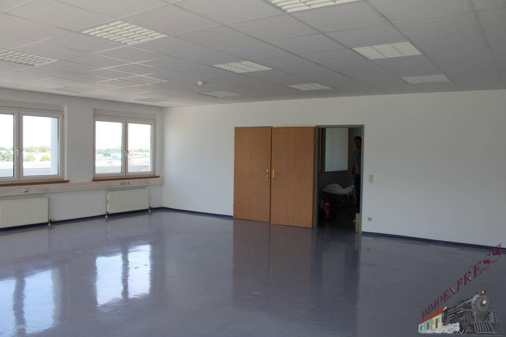 Großes Büro mit glänzendem Bodenbelag und Doppeltüren, die zu einem angrenzenden Bereich führen.