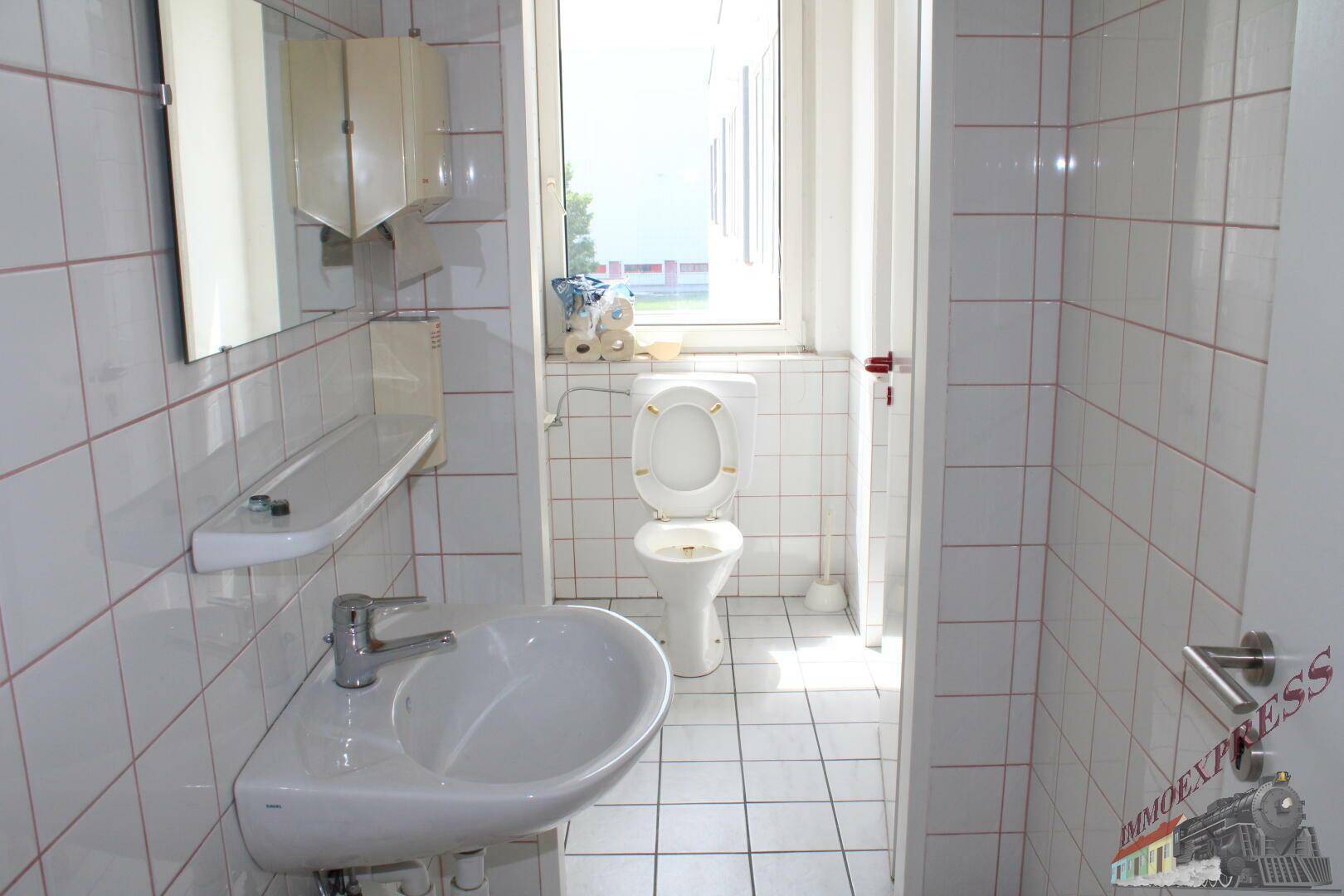 Helles WC mit Fenster, weiß gefliesten Wänden und einem Waschbecken.