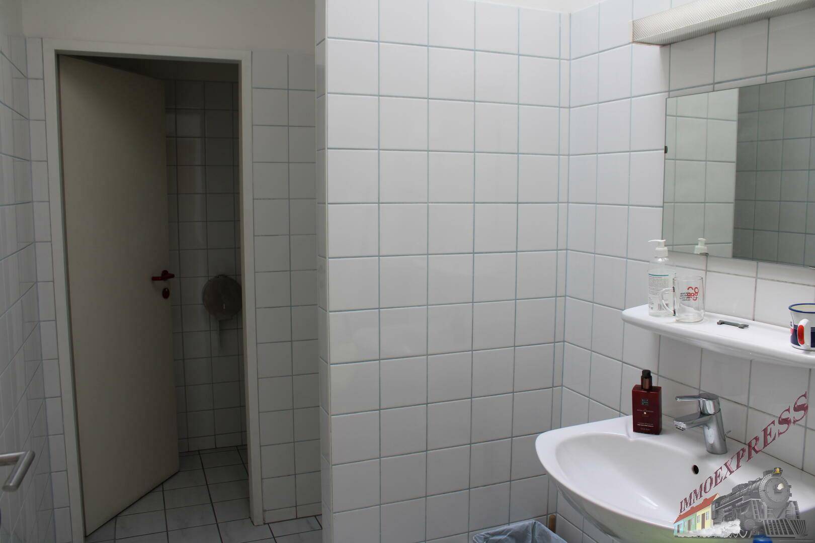 Badezimmer mit Waschbecken, Spiegel und Zugang zu einer Duschkabine, komplett gefliest.