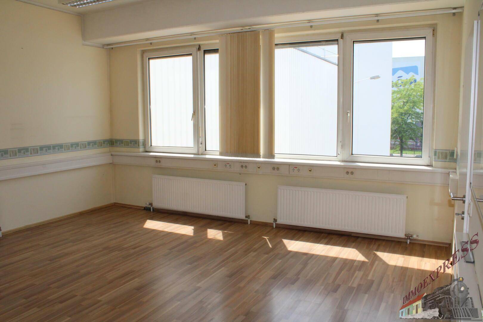 Büroraum mit Holzfußboden, großen Fenstern und viel natürlichem Lichteinfall.