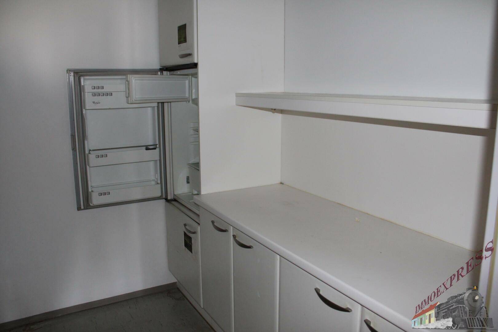 Kleine Küchenzeile mit weißen Schränken, Arbeitsplatte und integriertem Kühlschrank.