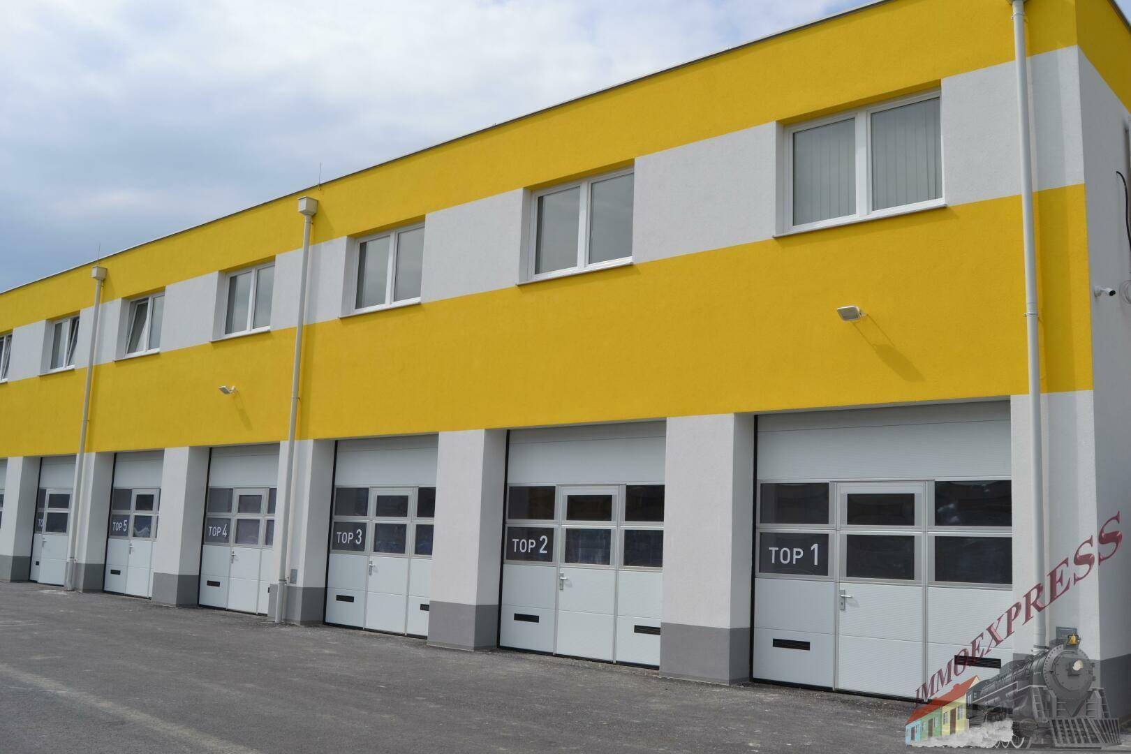 Gebäudeaußenansicht mit mehreren Garagentoren und gelb-weißer Fassade unter bewölktem Himmel.
