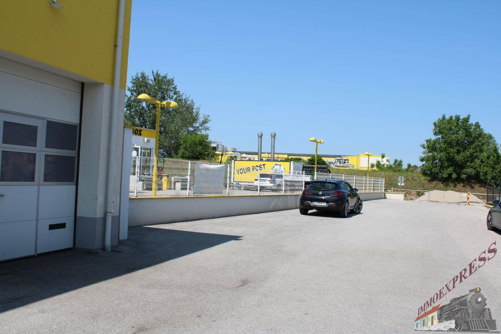 Außenbereich mit asphaltiertem Parkplatz neben dem Gebäude und Blick auf die Umgebung.