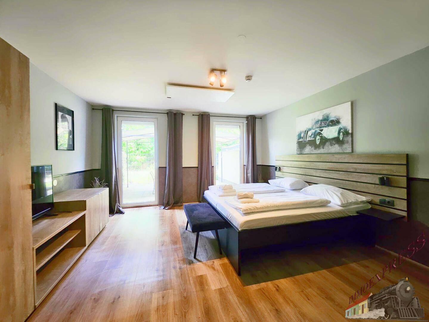Helles Schlafzimmer mit Holzboden, Doppelbett und Zugang zu einem Außenbereich.