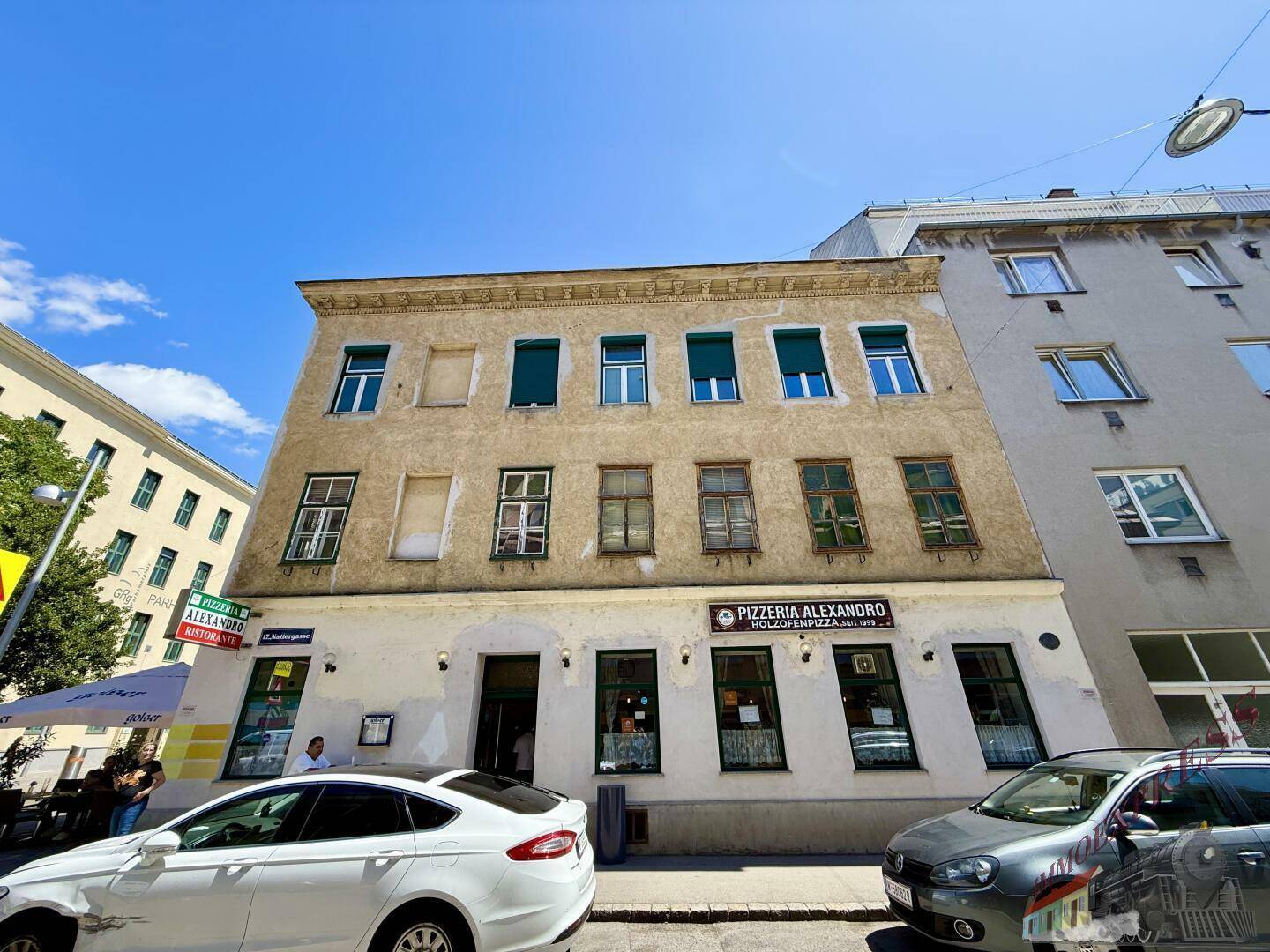 Frontansicht eines älteren Gebäudes mit einer Pizzeria im Erdgeschoss und mehreren Fenstern in den oberen Stockwerken.