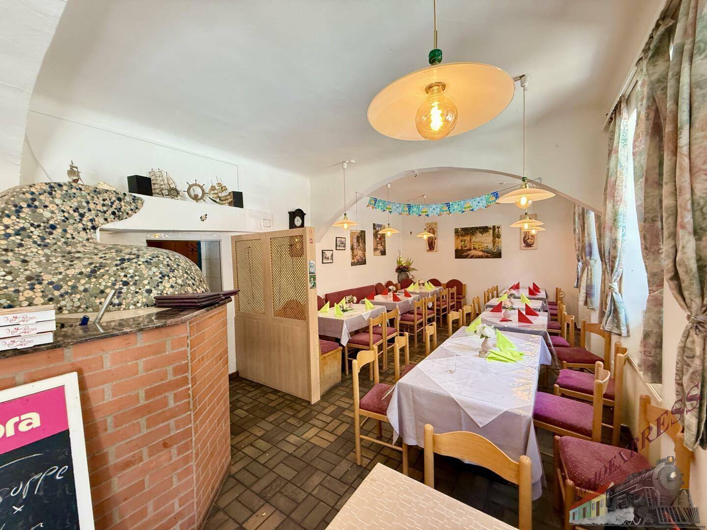 Gemütlicher Restaurant-Speisesaal mit traditionellen Holztischen, Stühlen und einem dekorativen Pizzaofen im Hintergrund.
