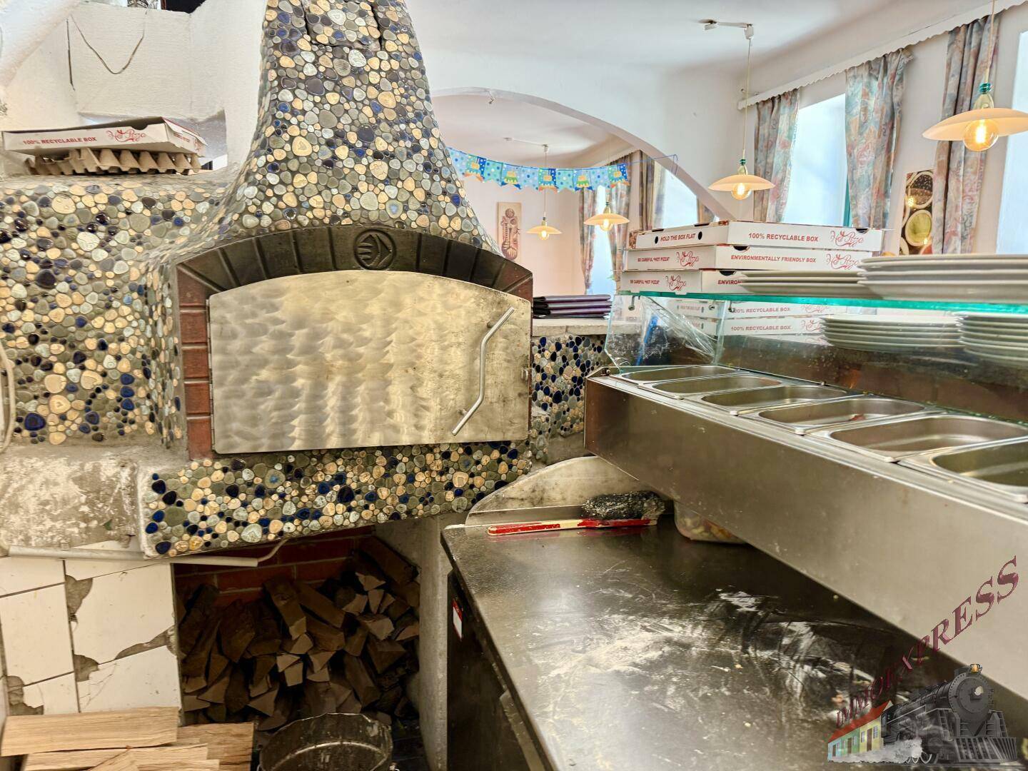Detailansicht eines großen, mit Mosaikfliesen verzierten Holzofen-Pizzaofens in einer professionellen Restaurantküche.
