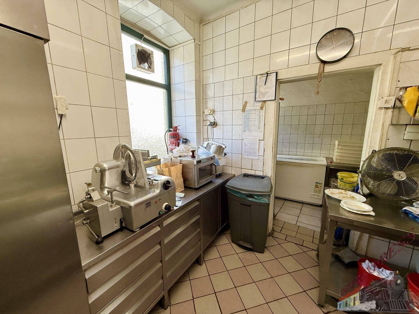 Professionelle Restaurantküche mit Edelstahlgeräten, Fliesenwänden und einem Fenster mit Abluftventilator.