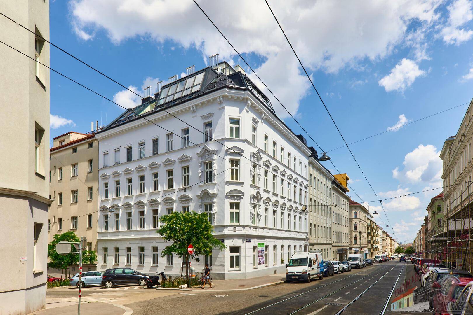 Historisches Eckgebäude mit moderner Dachaufstockung in einer belebten urbanen Umgebung.