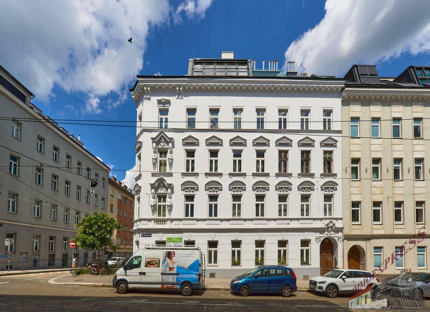 Historisches Eckgebäude mit moderner Dachaufstockung in einer belebten urbanen Umgebung.