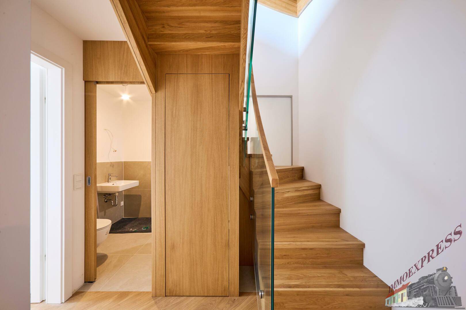 Flur mit Holztreppe und Zugang zu einem modernen Badezimmer mit WC.