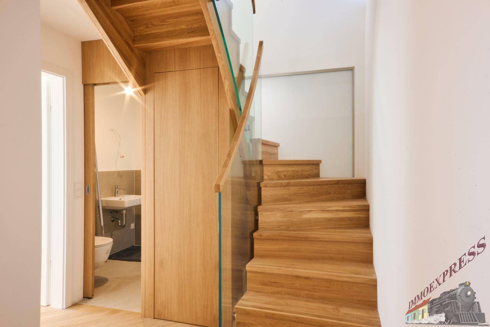 Flur mit Holztreppe und Zugang zu einem modernen Badezimmer mit WC.