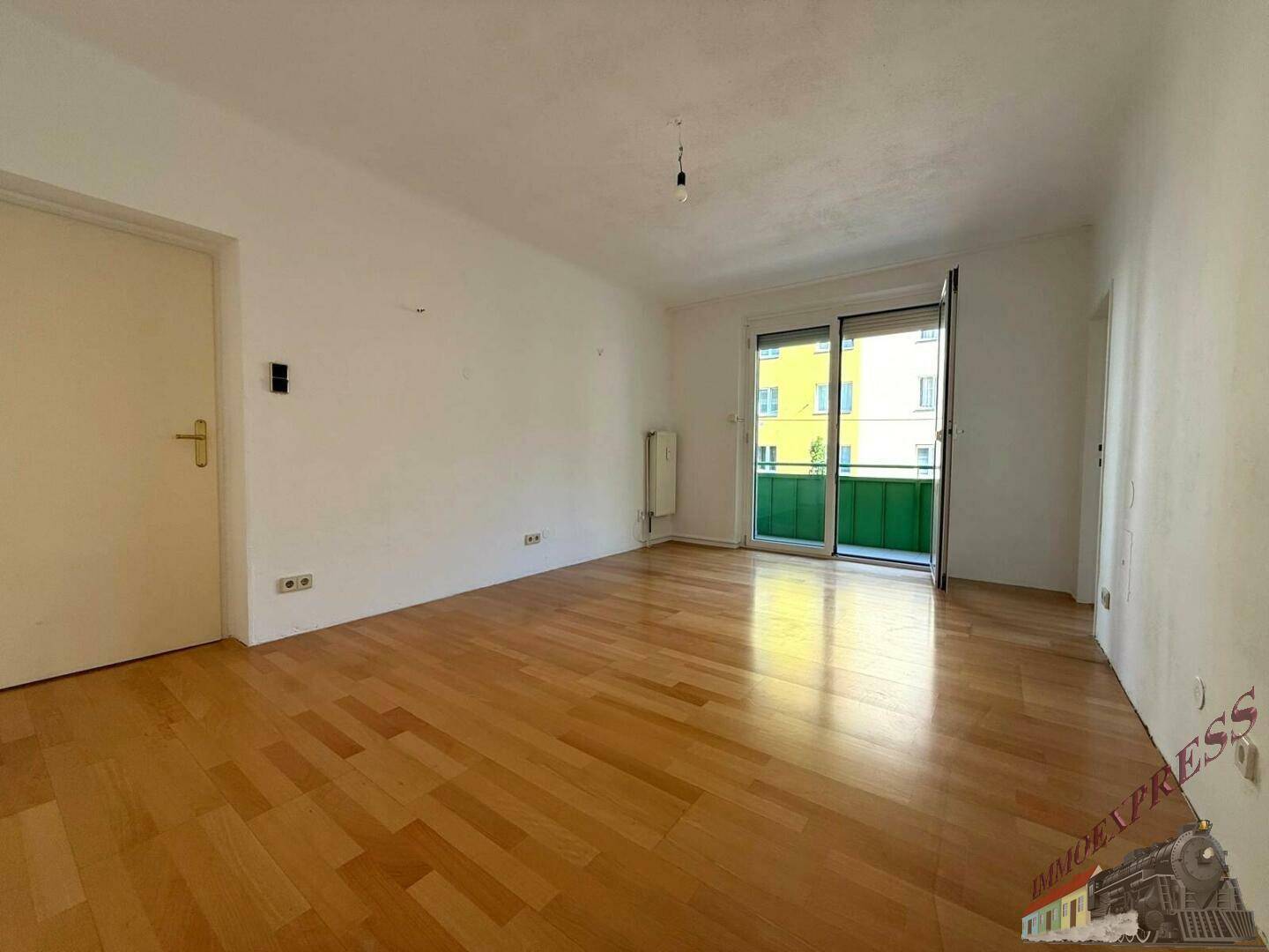 Heller Wohnbereich mit Parkettboden und Zugang zum Balkon, bietet eine angenehme Atmosphäre.
