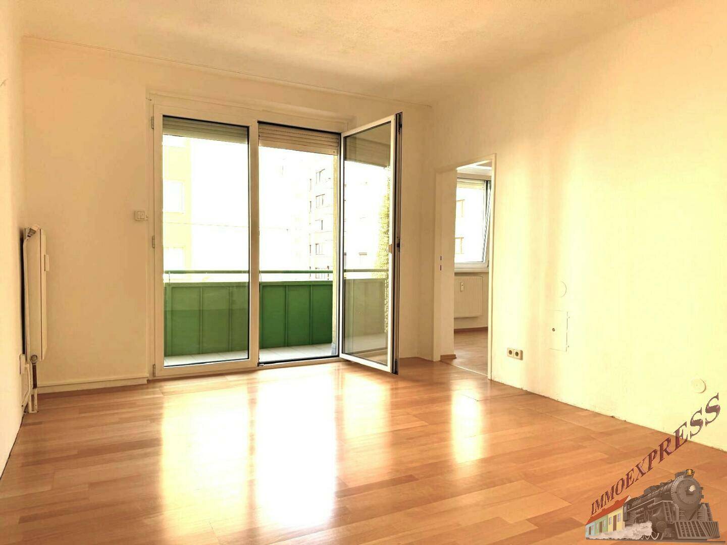 Geräumiges Wohnzimmer mit Holzboden und breiter Balkontür, die viel Licht hereinlässt.
