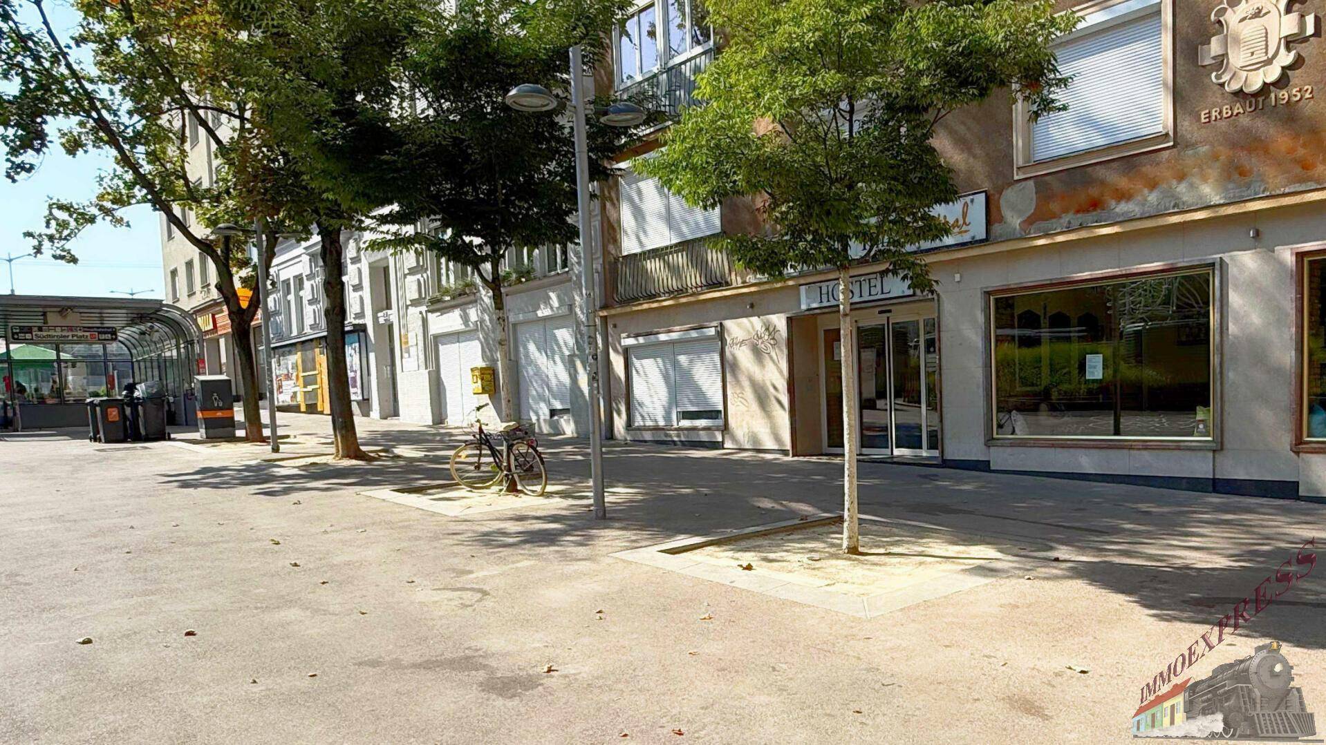 Außenansicht des Gebäudes an einer belebten Straße mit Geschäften und Bäumen, erbaut im Jahr 1952.