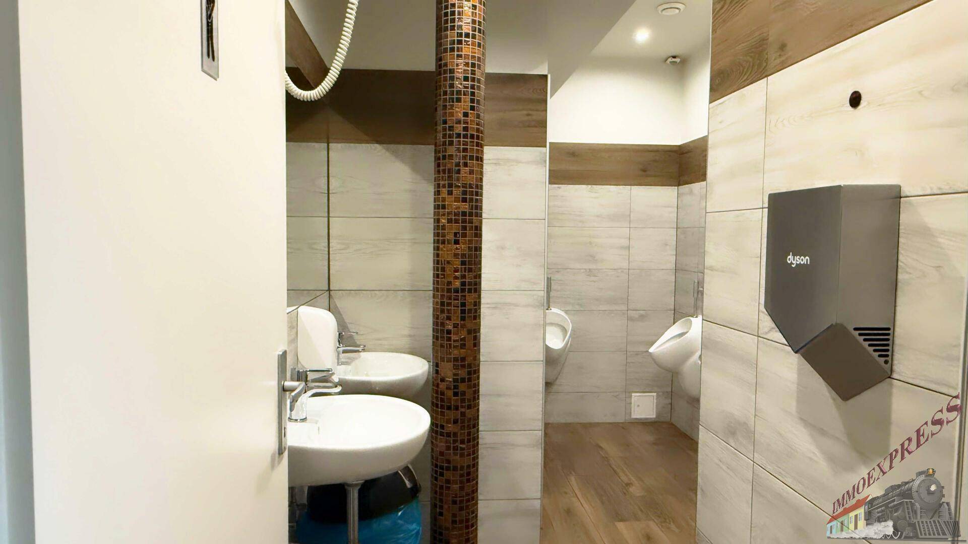 Öffentlicher Toilettenbereich mit mehreren Urinalen, Waschbecken und modernen Fliesen in Holzoptik.