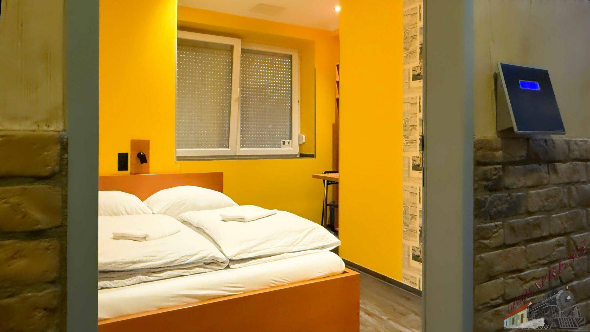 Schlafzimmer mit gelben Wänden, einem Doppelbett und einem Fenster mit Jalousien, das für Privatsphäre sorgt.