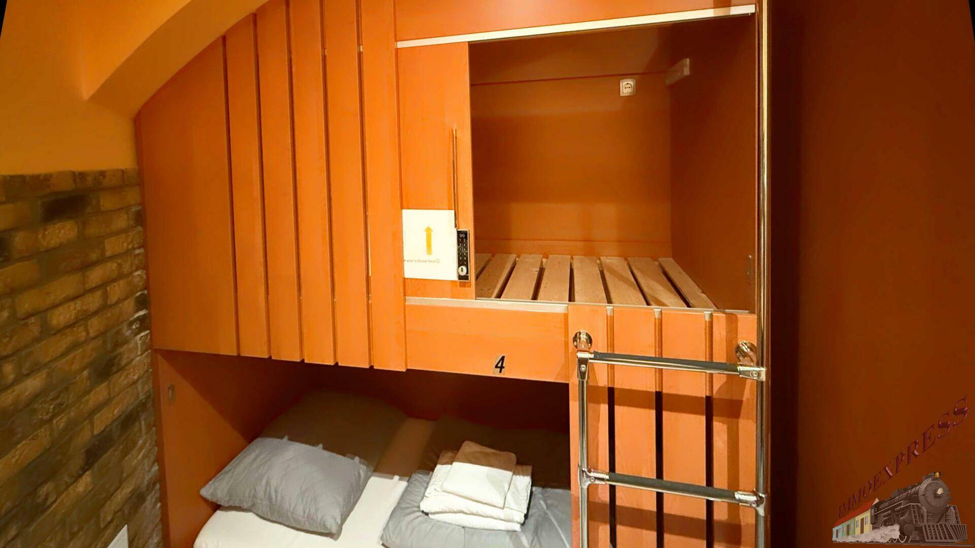Detailansicht eines orangefarbenen Kojenbettes mit Leiter und Stauraum, optimiert für Hostelgäste.