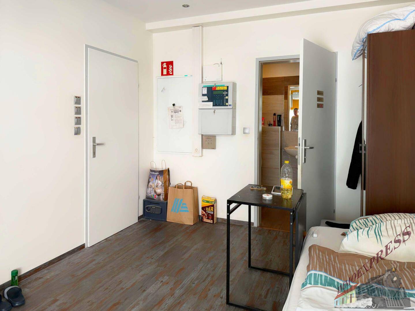 Schlafzimmer mit Holzboden und einfacher Einrichtung, inklusive eines Tisches und eines Kleiderschranks.