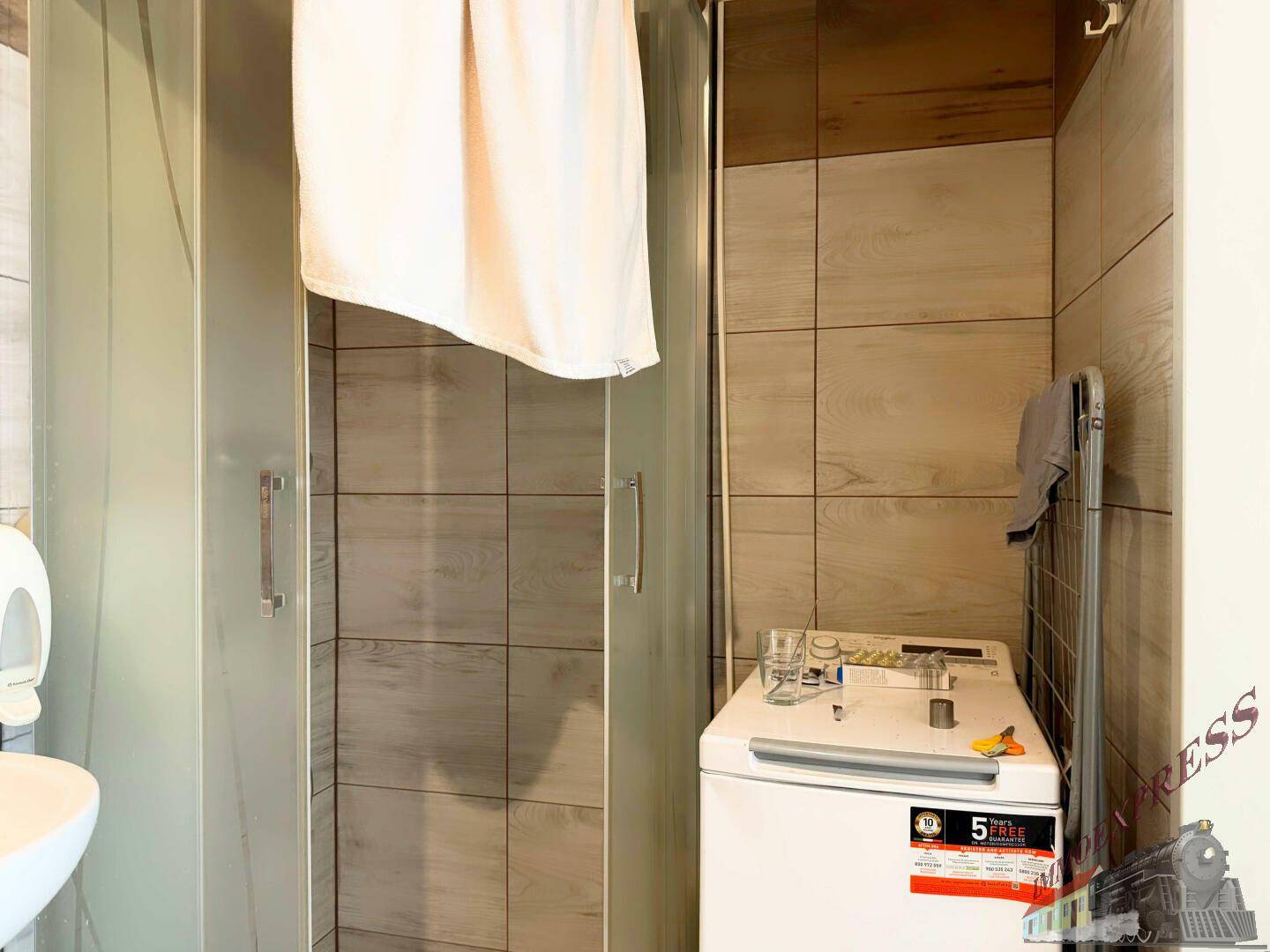 Badezimmer mit Duschkabine, Waschmaschine und Fliesen in Holzoptik, praktisch und funktional eingerichtet.