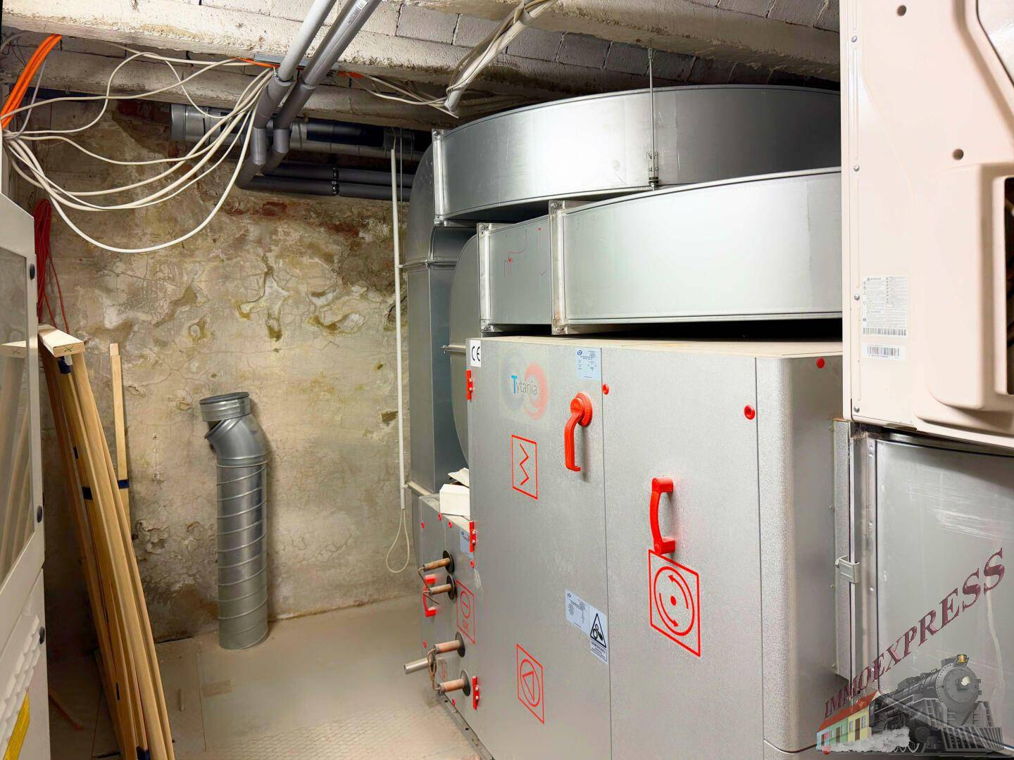 Technischer Raum im Keller mit umfangreicher Lüftungsanlage und sichtbaren Kabeln und Rohren.