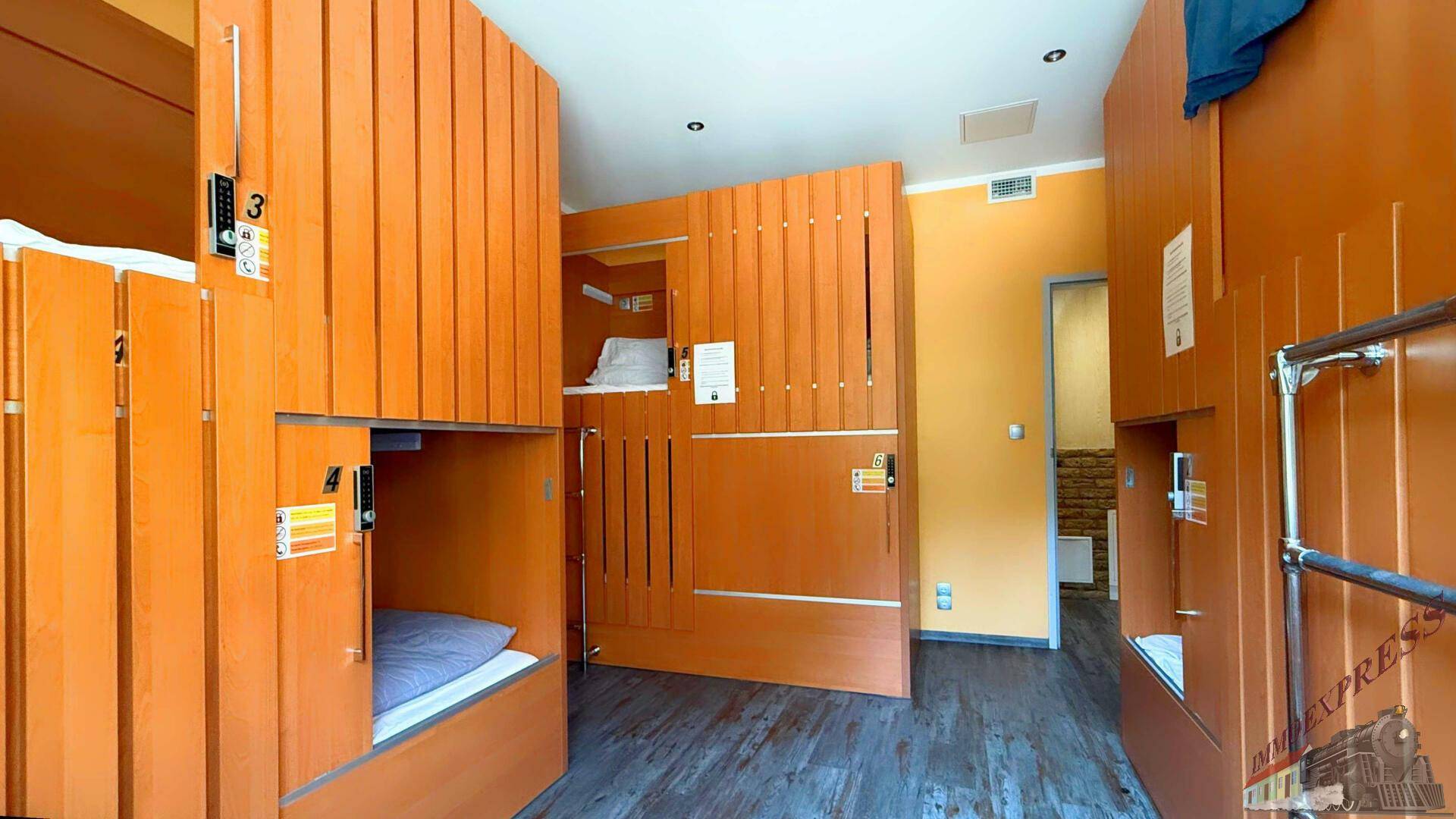 Schlafraum mit mehreren orangefarbenen Kojenbetten und Holzboden, ideal für Hostelgäste.