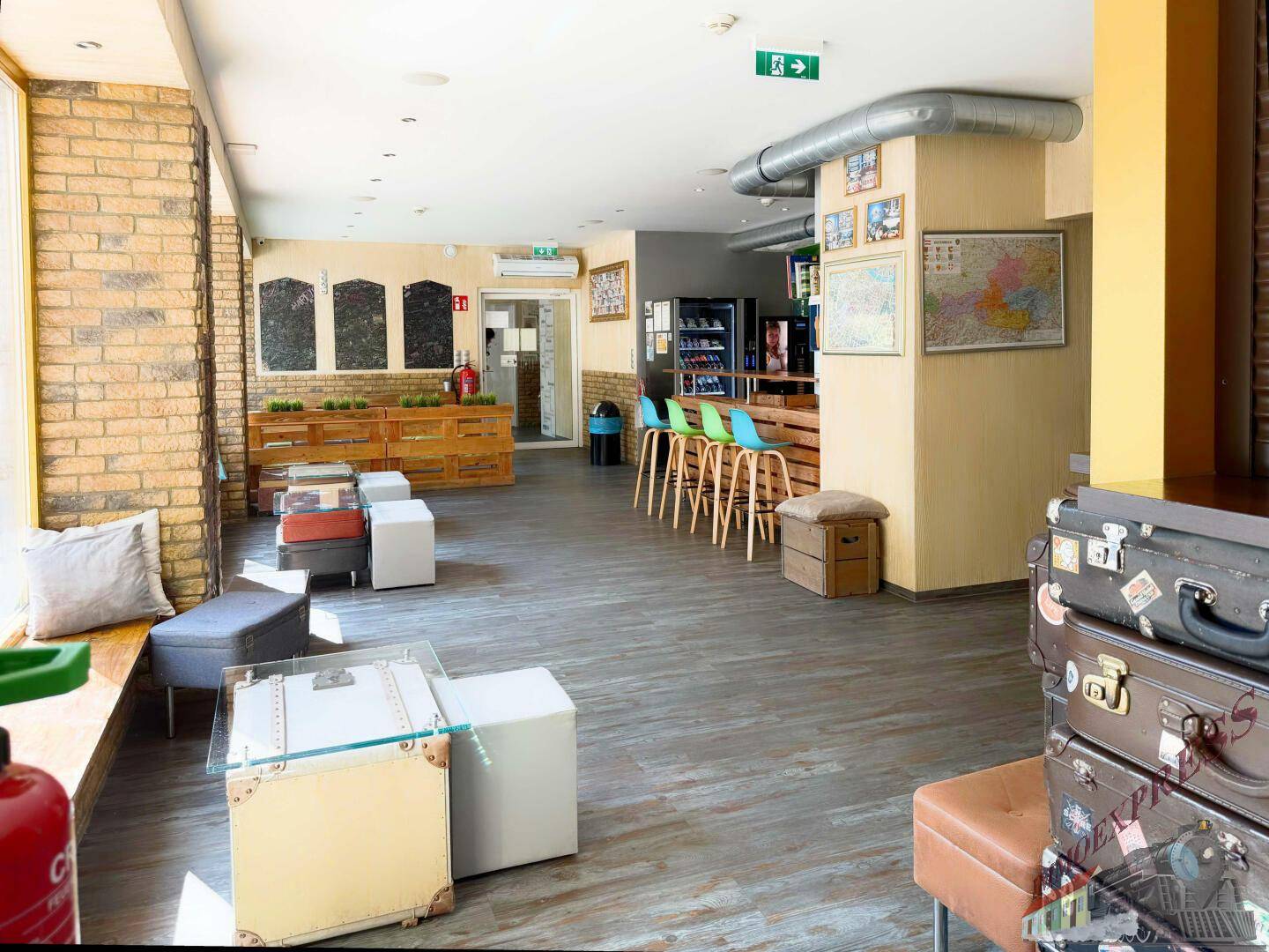 Geräumiger Gemeinschaftsbereich mit Holzboden, Ziegelwänden und verschiedenen Sitzgelegenheiten, inklusive einer Bar im Hintergrund.