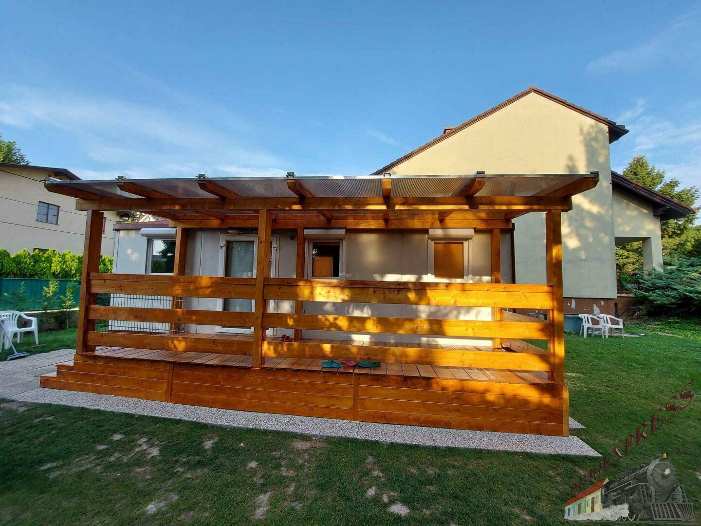 Geräumige überdachte Holzterrasse mit transparentem Dach und Blick auf das Wohnhaus.