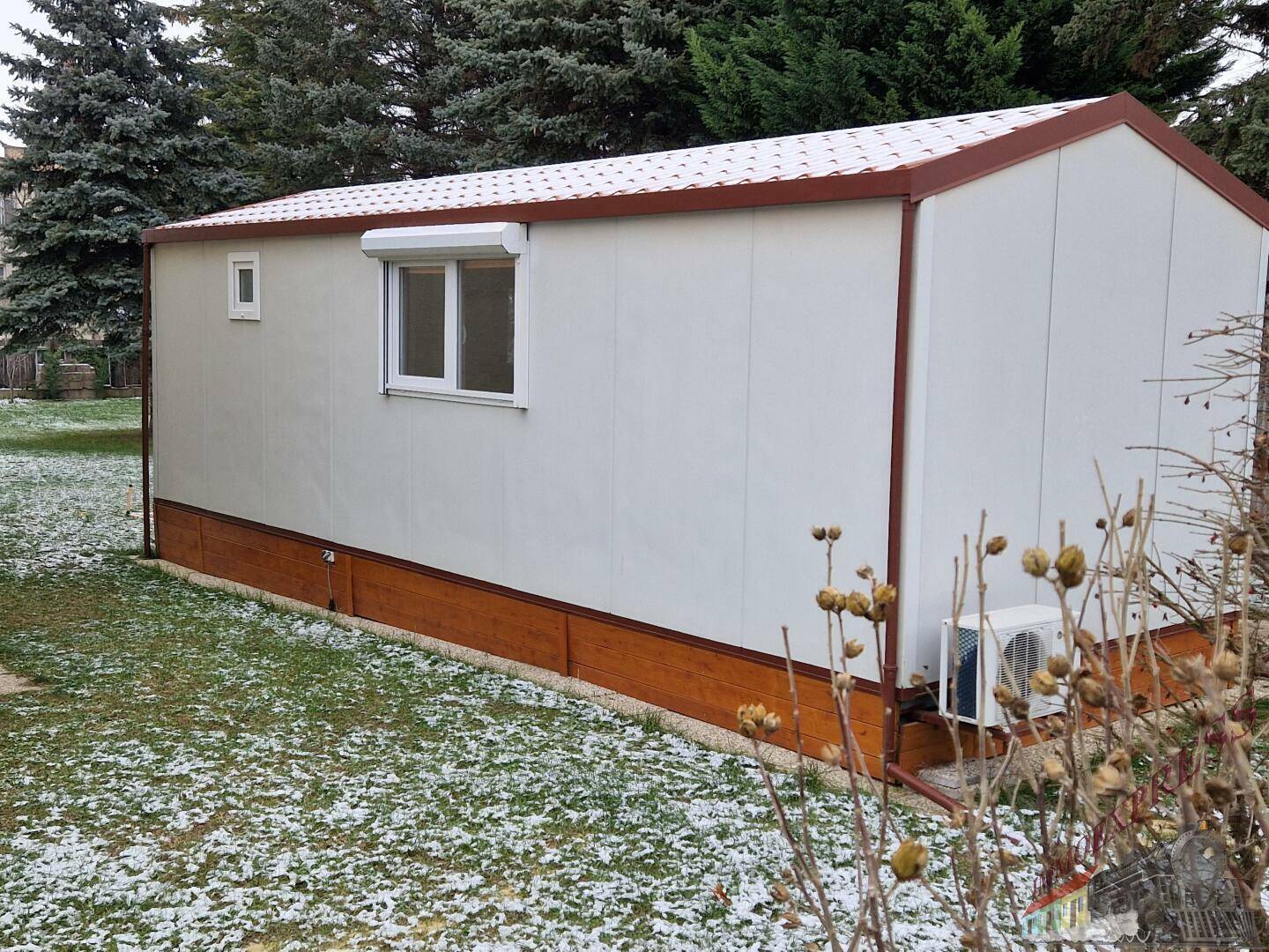 Kleines Fertighaus mit Rollläden und Klimaanlage in winterlicher Umgebung.