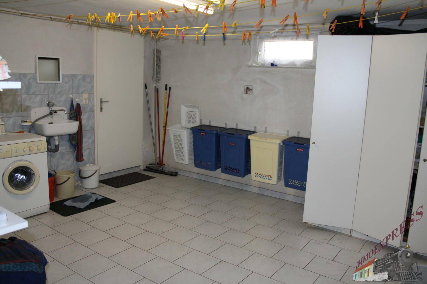 Geräumiger Waschraum im Keller mit Waschmaschine, Spülbecken und Wäscheleinen.